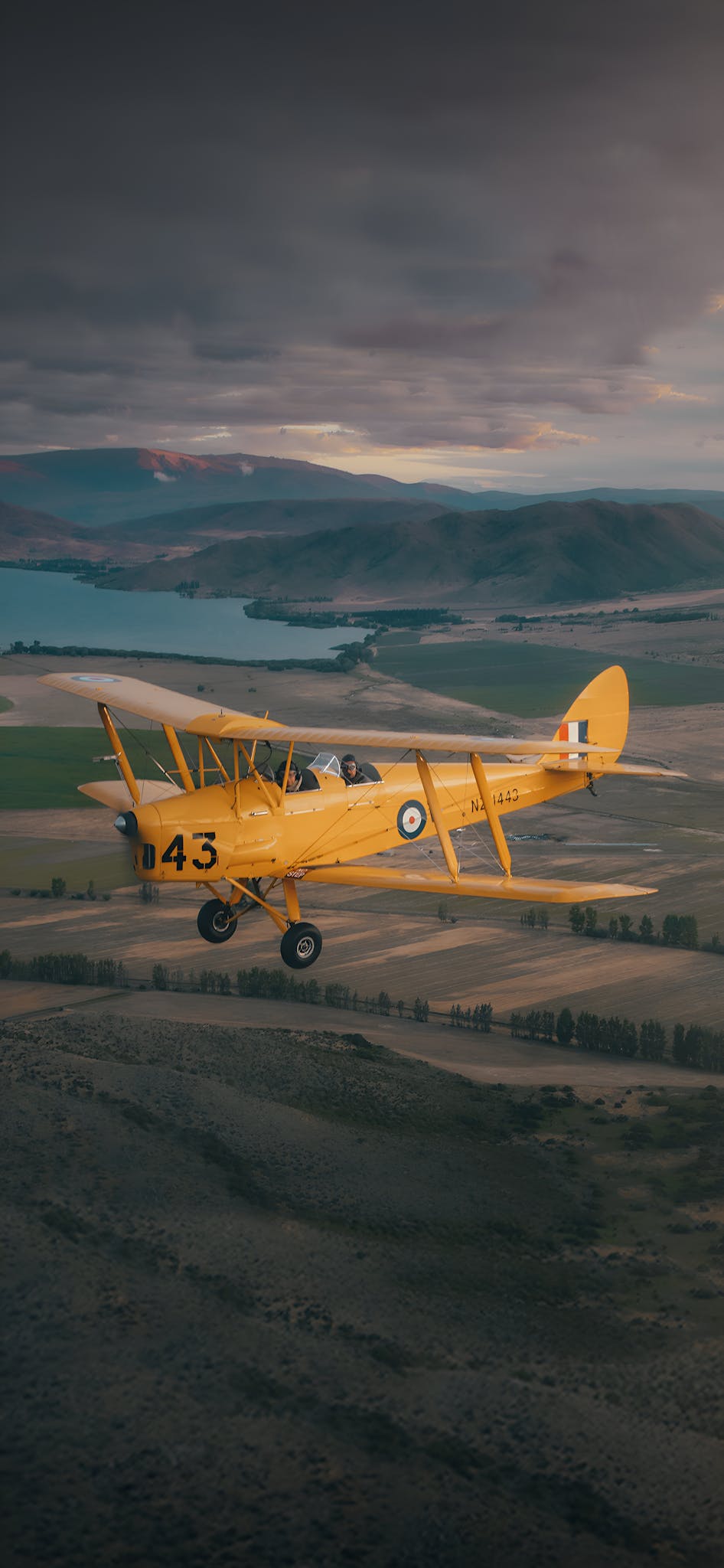 A classic yellow biplane soaring over Aoraki / Mount Cook's scenic landscape under dramatic skies.