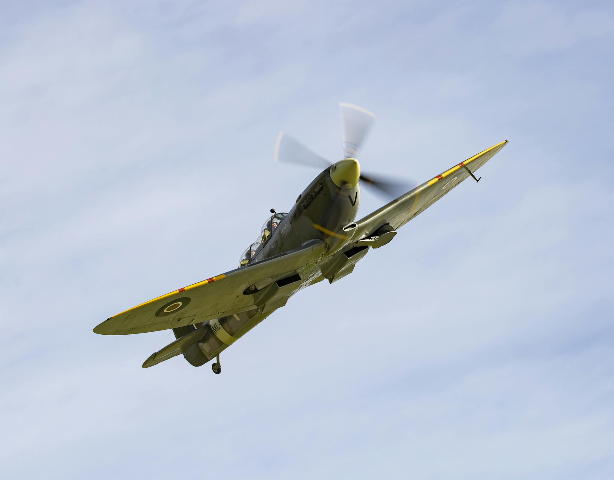 A vintage fighter plane soars through a clear blue sky, showcasing historic aviation design.