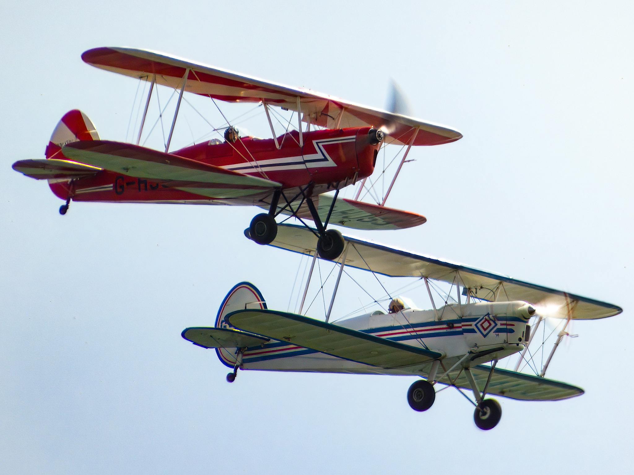 Two vintage biplanes performing an aerobatic display against a clear blue sky.